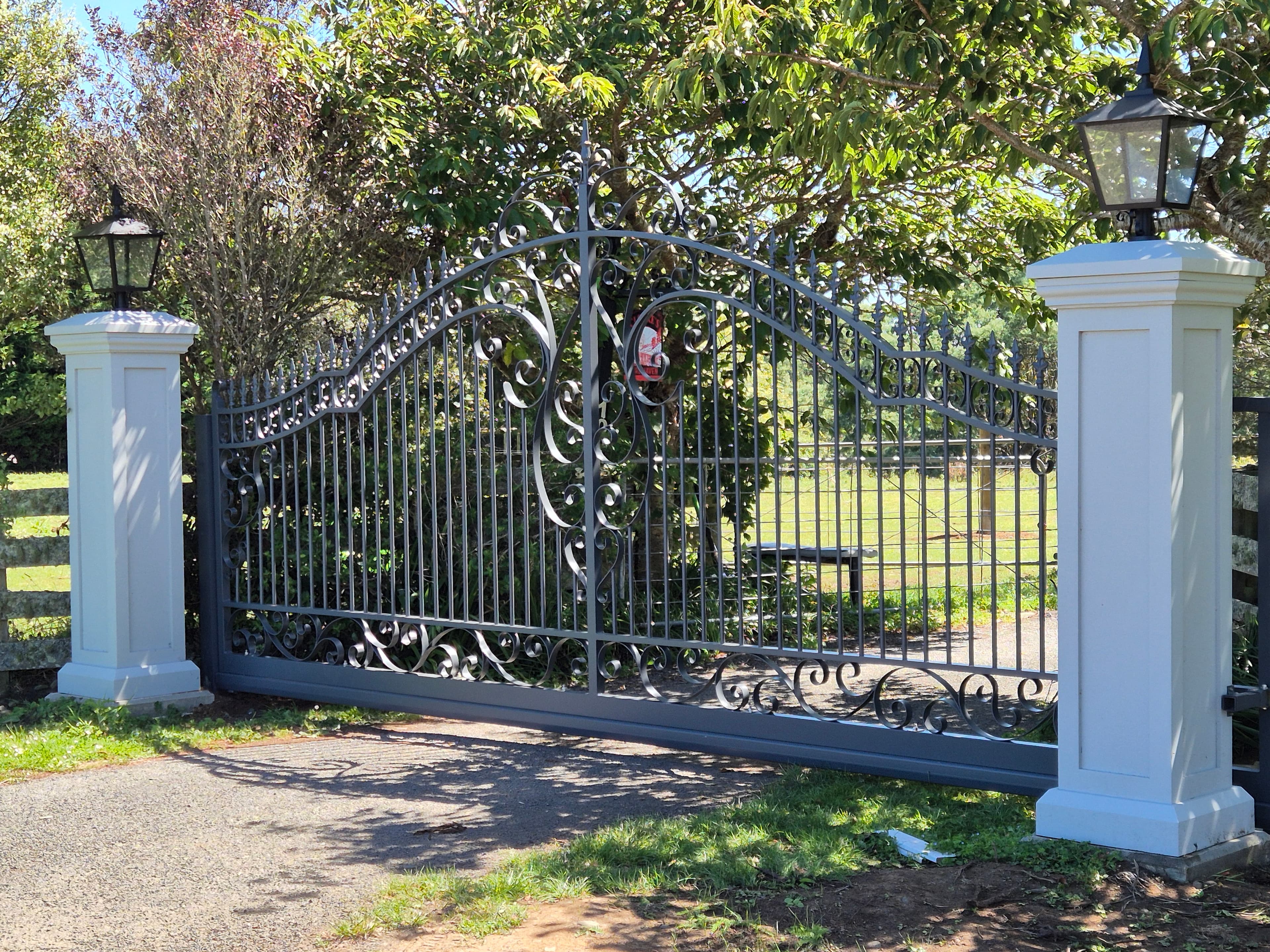 Ornate wrought iron driveway gate flanked by white pillars