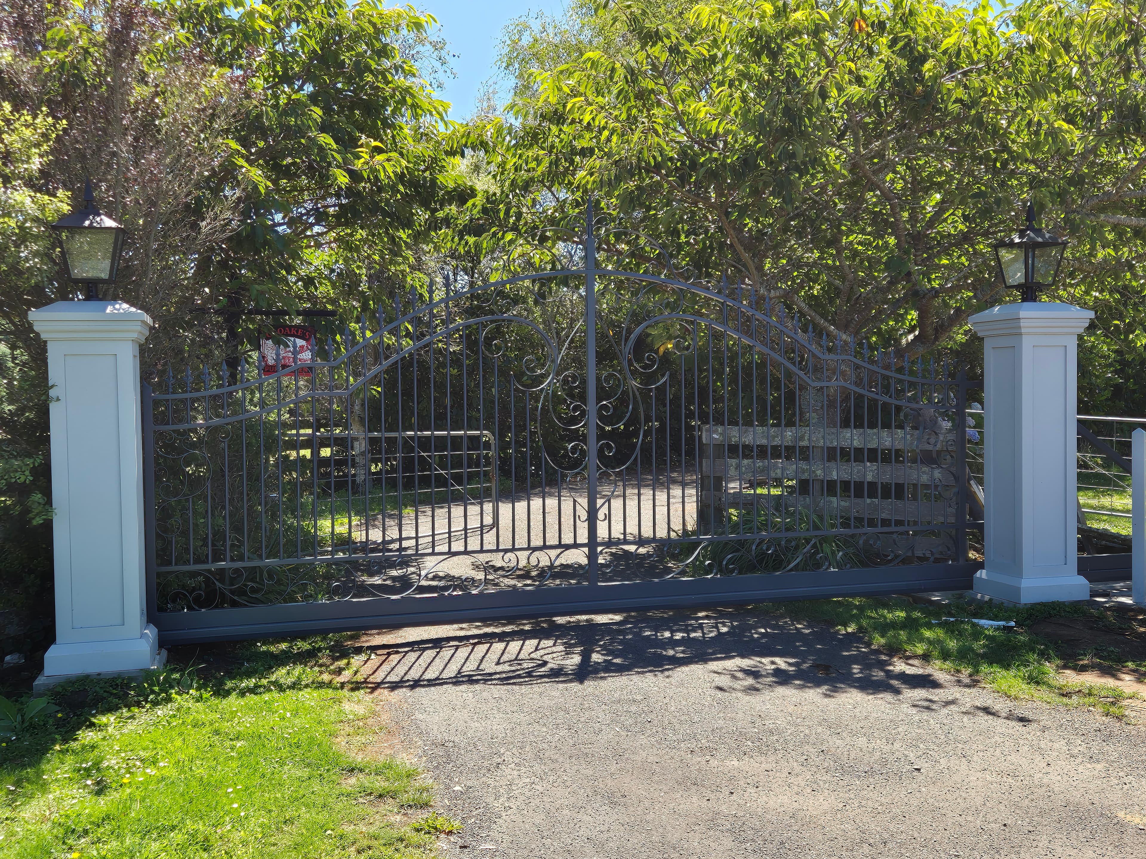 Ornate scroll driveway gate between white entrance pillars