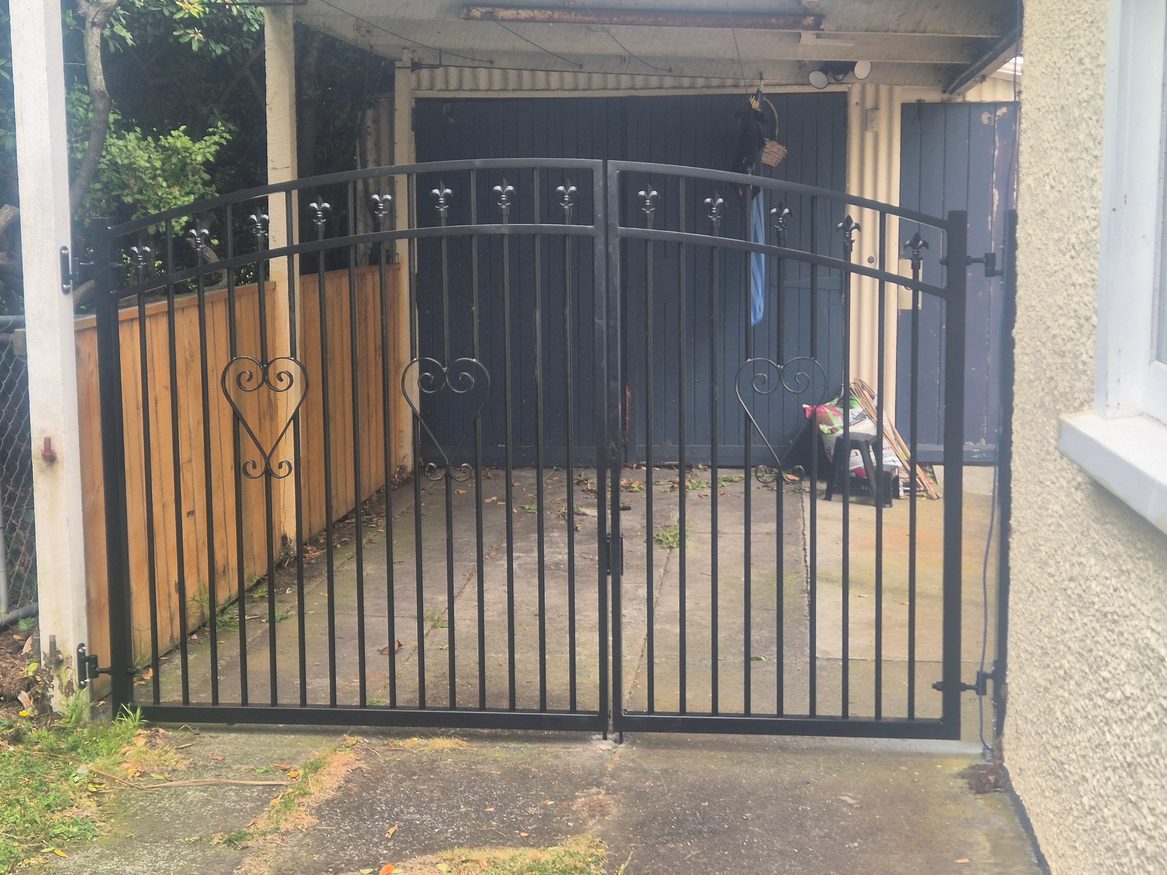Black arched gate with heart scrollwork at a carport entrance