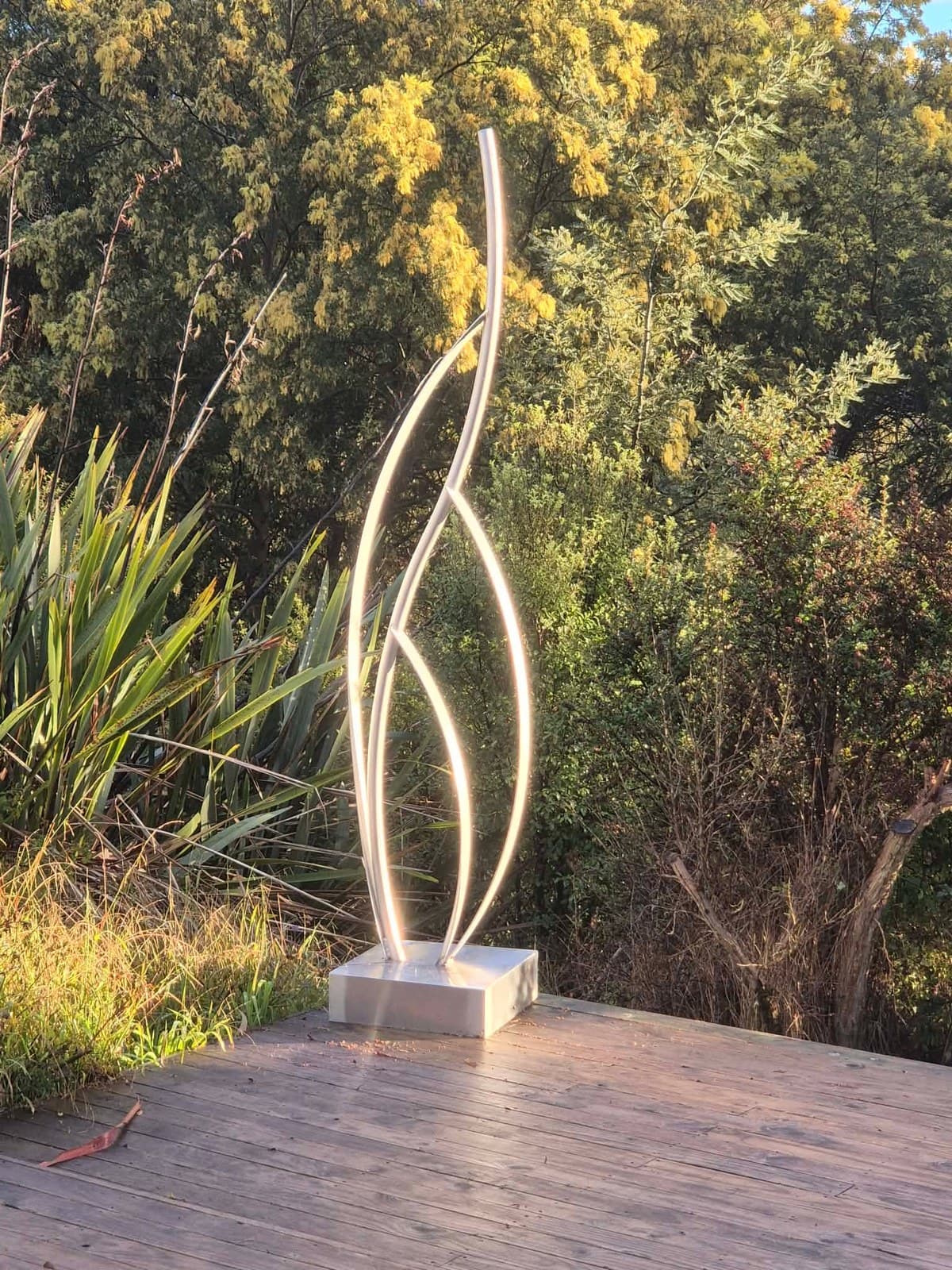 Illuminated flame-shaped stainless steel sculpture on an outdoor deck at dusk