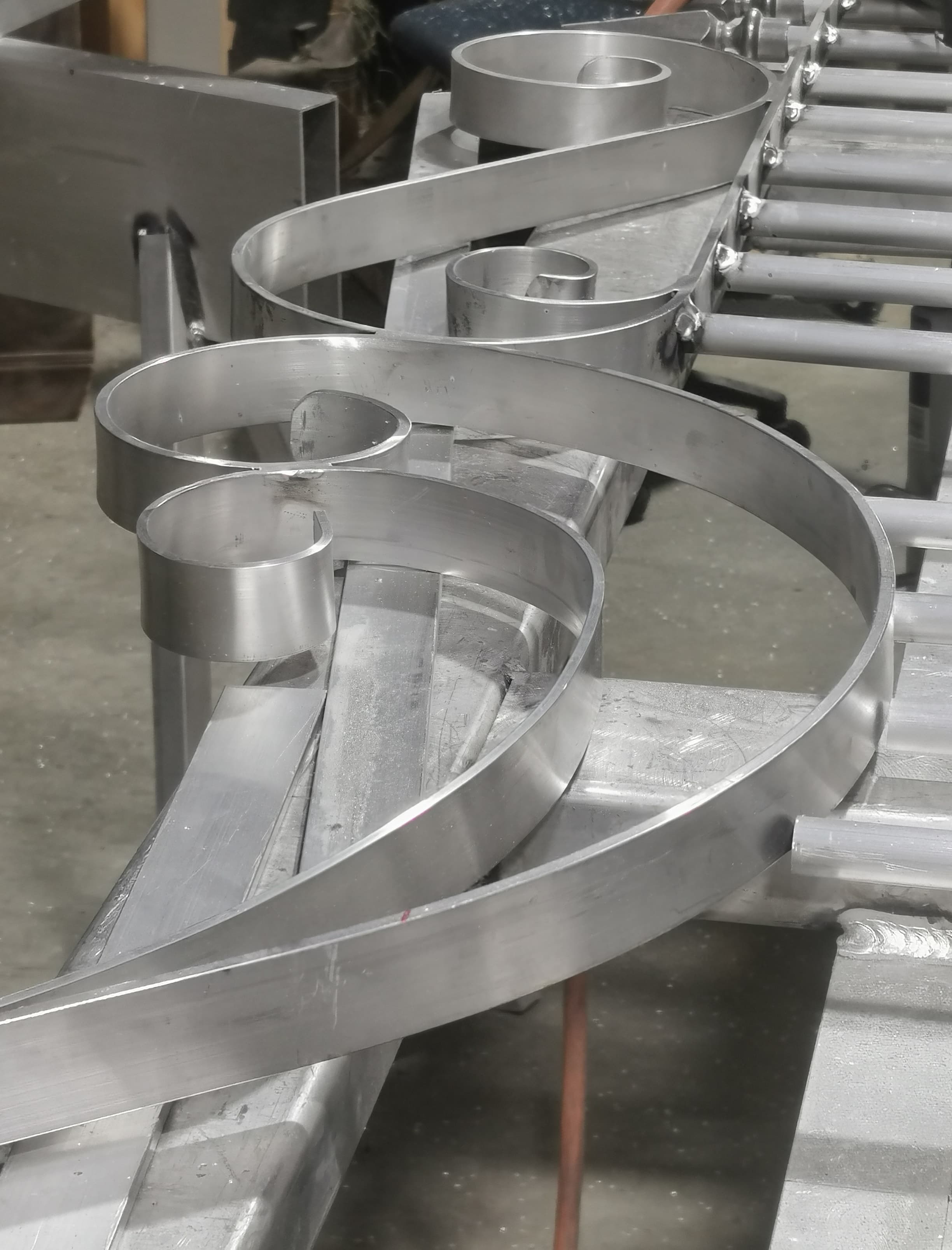 Stainless steel ribbon sculpture taking shape on the workshop bench